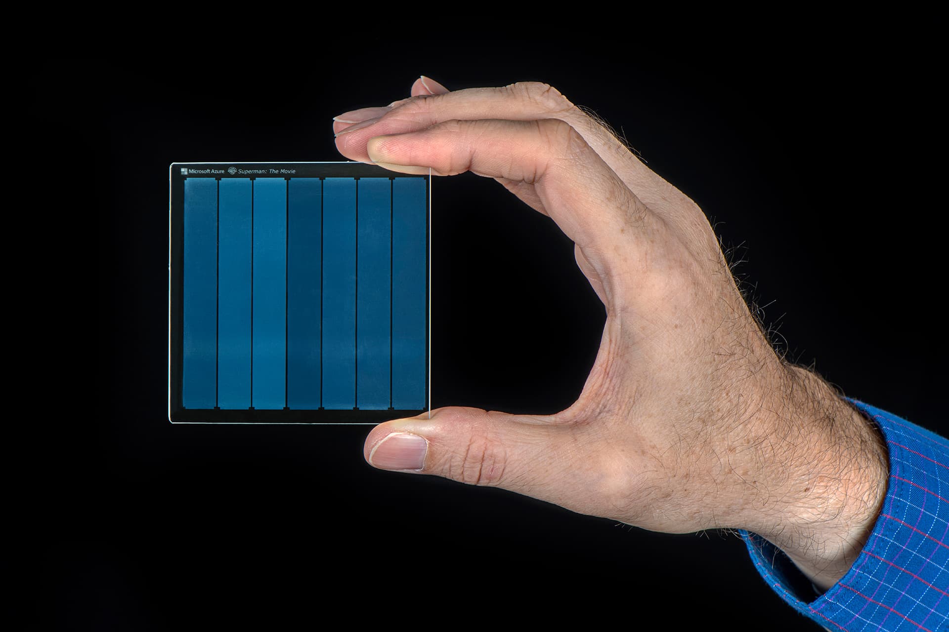 A hand holding a small square of quartz glass with data etched inside it